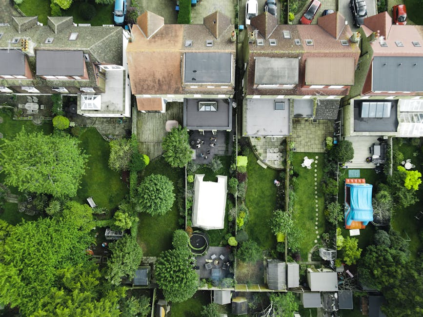An aerial view of a row of terraced houses with adjacent gardens showing a variety of maintenance stages and garden features; some gardens have well-manicured lawns with neatly trimmed grass, while ot